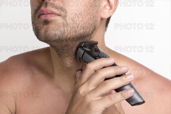 Portrait young man shaving his beard with electric shaver