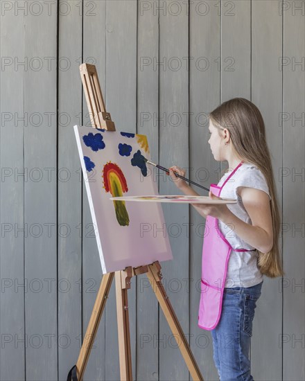 Side view girl drawing with paint brush easel against wooden plank