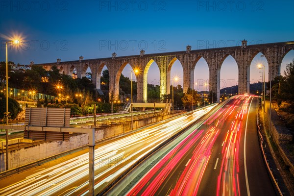 View of highway traffic near Campolide station with Aguas Livres Aqueduct in background in the evening with car lights trails. Lisbon