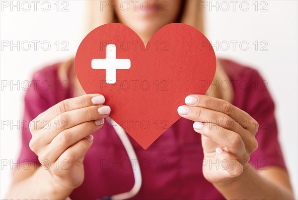 Defocused female doctor holding paper heart