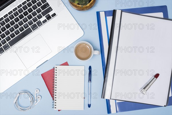 High angle view laptop folders coffee cup earphone spiral notepad pen against blue background