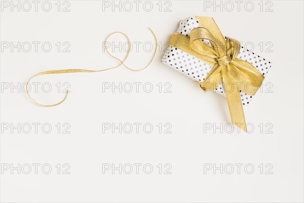 Elevated view present box wrapped polka dot design paper with shiny golden ribbon isolated white backdrop