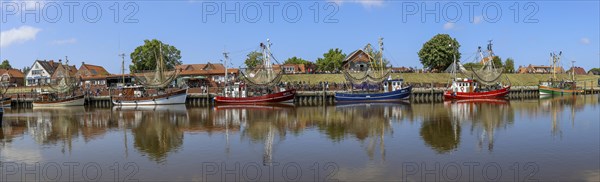 Panorama photo crab cutter with reflection in the water in the harbour of Greetsiel with historical houses