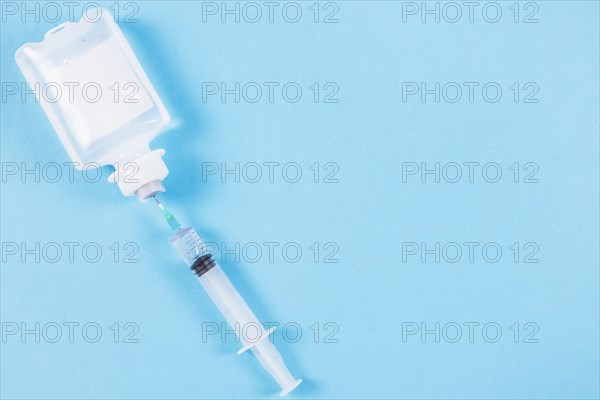 Syringe inserted normal saline solution plastic bottle blue background