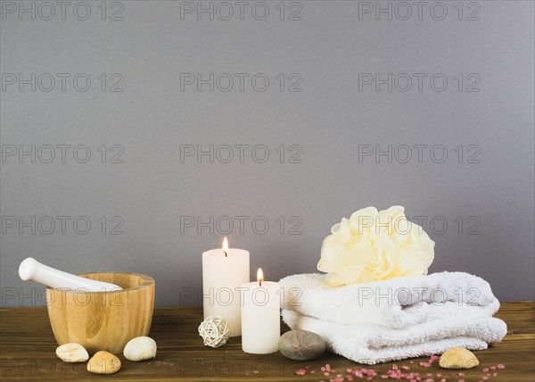 Illuminated candles towel spa stones loofah mortar pestle wooden surface