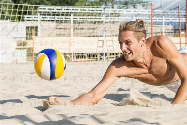 Side view shirtless man reaching hit volleyball before it hits sand