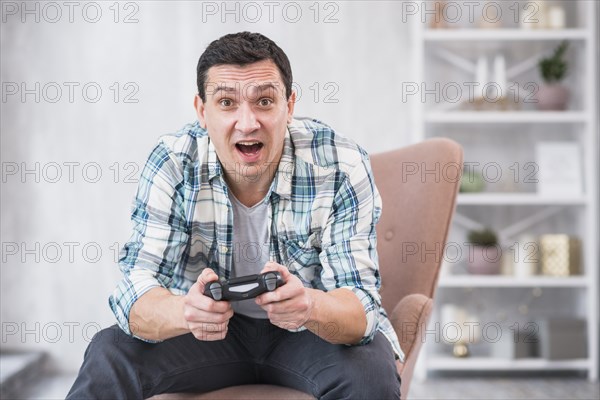 Excited young male sitting armchair playing with gamepad