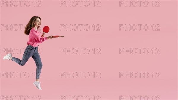 Portrait happy woman jumping with ping pong paddle