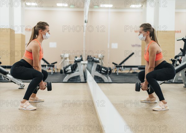 Woman gym training with medical mask front mirror