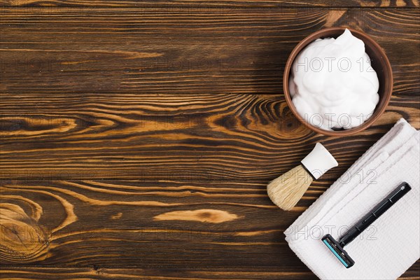 Overhead view foam bowl shaving brush razor white folded napkin against wooden textured backdrop