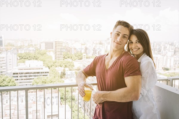 Happy woman hugging man with juice glass balcony