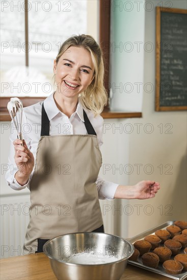 Smiling young woman holding cream with whisk coffee shop