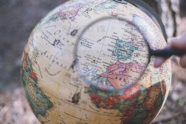 Person with magnifying glass looking globe