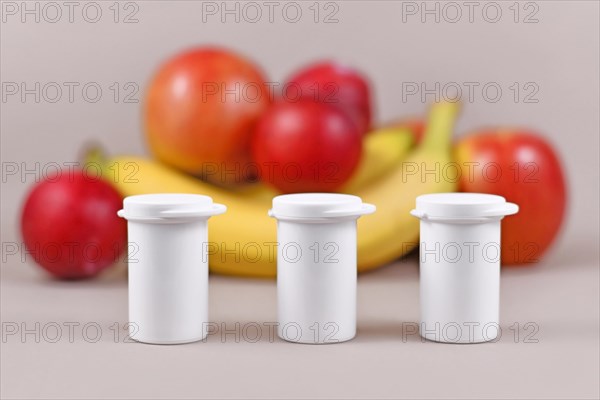 Small bottles with food nutrition supplements in front of fruits and vegetables in blurry blue background