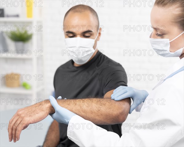 Female physiotherapist with medical mask checking man s elbow