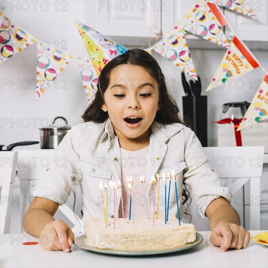 Surprised birthday girl blowing cake with illuminated candles