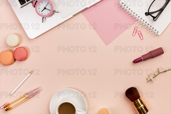 Macaroons coffee cup makeup brushes alarm clock laptop peach colored background