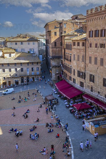 Tourists rest on the Piazza del Campo or sit in street cafes under red awnings