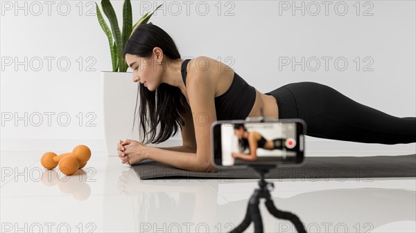 Female influencer home vlogging while exercising with smartphone