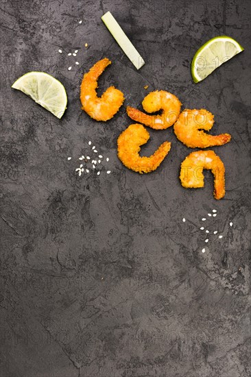 Golden fried shrimps with sesame seeds lemon wedges rough black surface