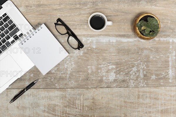 Laptop spiral notepad eye glasses black tea plant wooden table