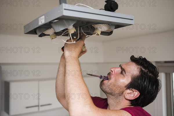 Man carrying tester mouth while repairing ceiling focus light home