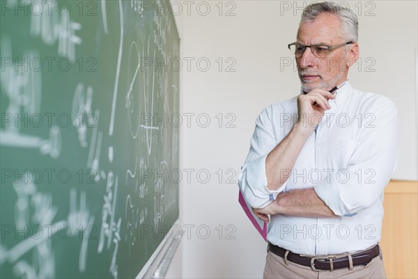Aged math teacher thinking chalkboard