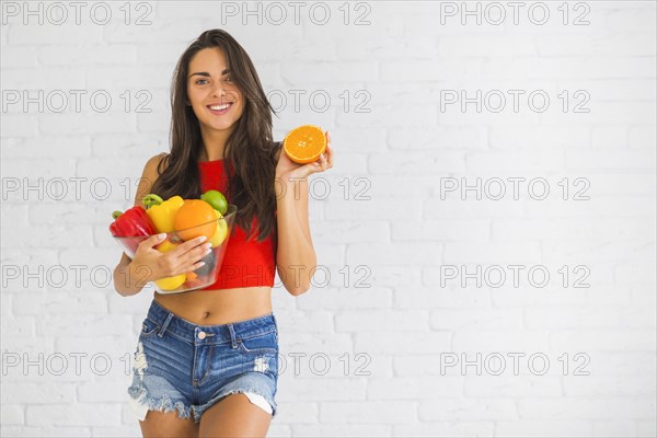 Smiling woman standing against wall holding fresh vegetable fruits