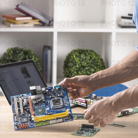 Close up male technician holding modern computer motherboard from table