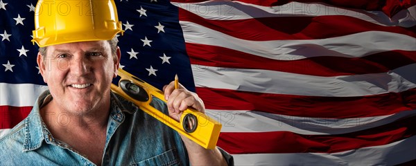 Male contractor wearing blank yellow hardhat over waving american flag background banner