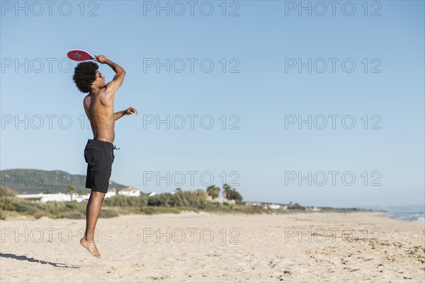 Man jumping with tennis racket beach