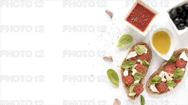 Bruschetta with cheese tomato basil leaves topping near sauce olives oil garlic clove white surface