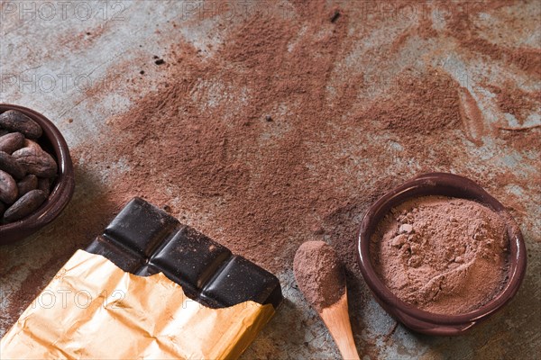 Dark chocolate bar with scattered cocoa powder beans bowl rustic backdrop