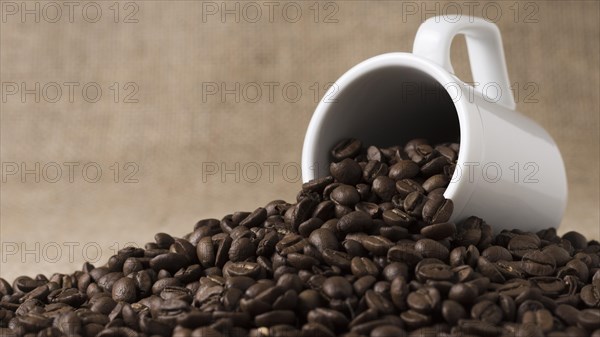 Front view roasted coffee beans spilled from white mug