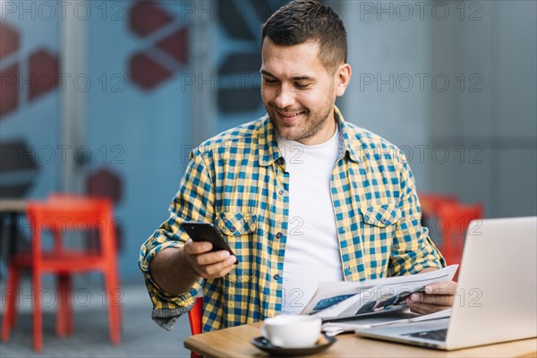 Man with laptop using smartphone cafe