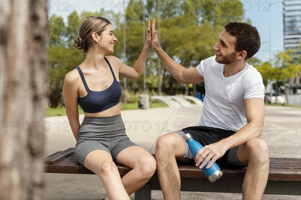 Front view man woman resting outdoors after exercising giving each other high five