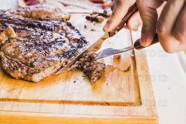 Close up person s hand slicing meat with fork knife