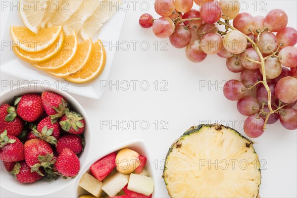 Slices citrus fruit strawberry pineapple watermelon grapes white backdrop