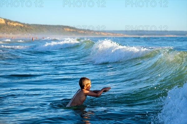 Boy has fun enjoys jumps dives in ocean sea waves of Atlantic Ocean. Fonta da Telha beach