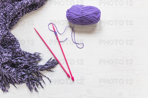 Knitted needles with purple yarn scarf white textured backdrop