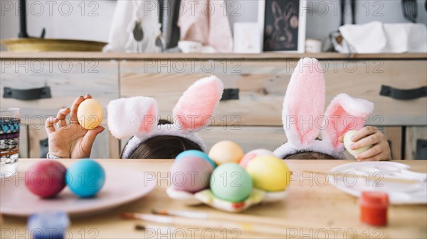 Mother with child bunny ears hiding table with colored eggs
