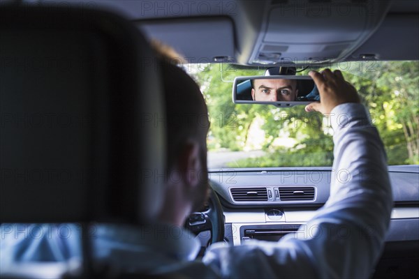 Man sitting inside car adjusting rear view mirror