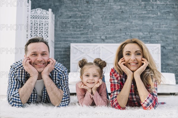 Joyful cute family lying carpet looking camera