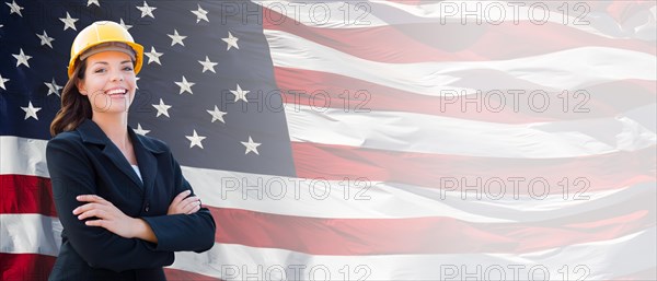 Female contractor wearing blank yellow hardhat and suit over waving american flag background banner