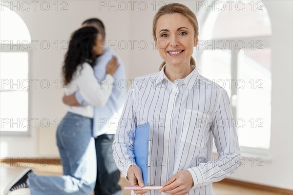 Front view smiley female realtor with young couple embracing background