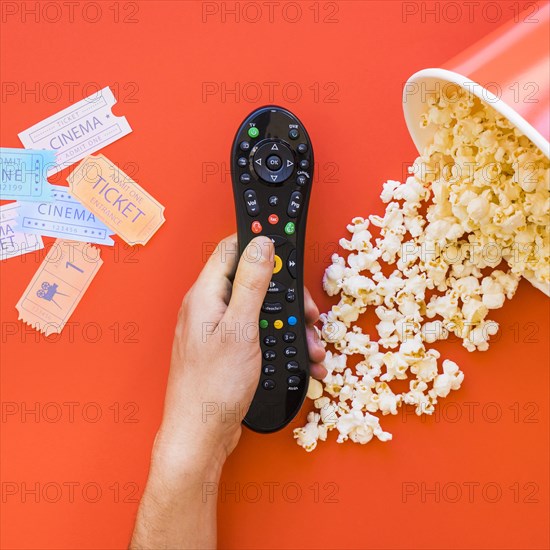 Hand holding remote control popcorn movie tickets