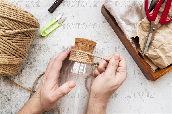 Close up person wrapping jute string glass bottle white textured backdrop