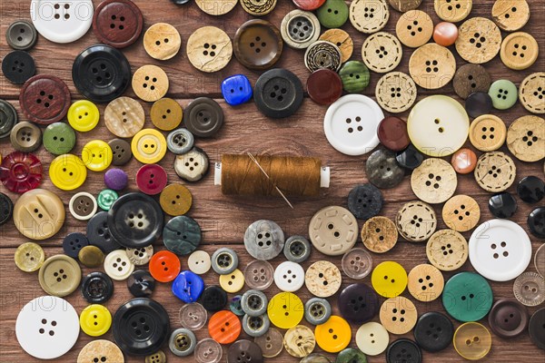 Many colorful buttons brown thread needle wooden background