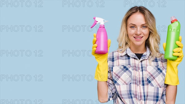 Front view happy woman looking camera holding spray bottle detergent bottle