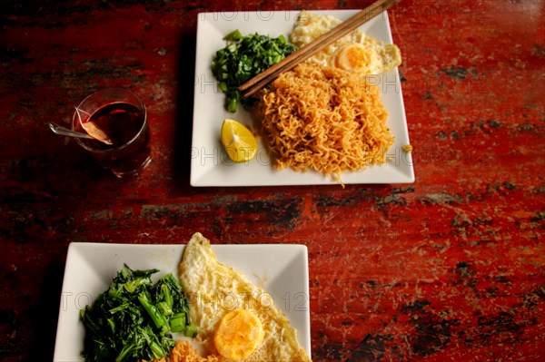 Stir fried wonton noodles with fried egg and spinach against a rustic red table